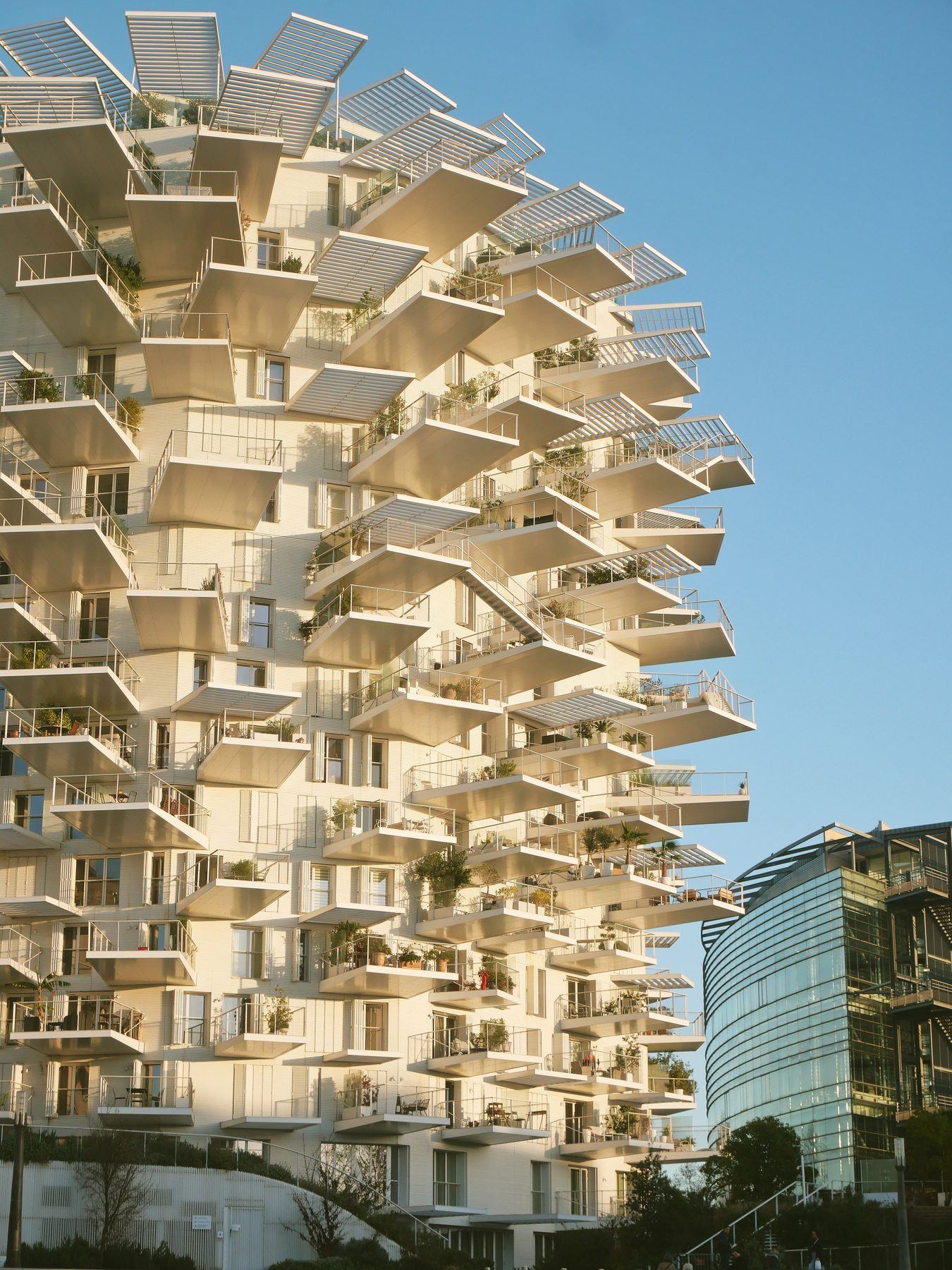 Edifício residencial branco com varandas escalonadas e árvores plantadas nos terraços